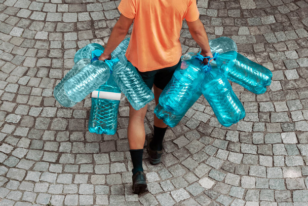 Young man carries many disposable plastic bins to trash can. Single use plastic pollution. Waste collection, recycling and sorting. Ecology, environmental issues concept - 写真・画像