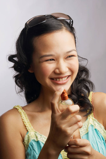 Close-up of a young woman holding a bottle of perfume and smiling - Photo, image