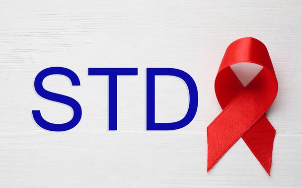 Red awareness ribbon and abbreviation STD on white wooden background, top view  - Valokuva, kuva