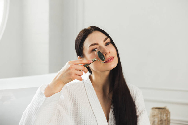 Beautiful european woman uses jade roller to massage her face. Spa self beauty procedure - Foto, imagen