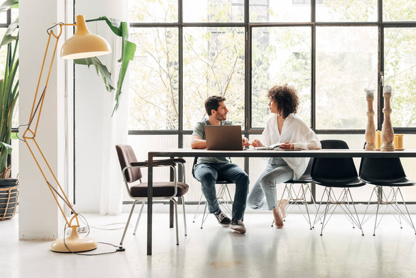Young multiracial colleagues sharing ideas in bright co working loft office. Huge window. Coworking concept. Business meeting concept. Startup concept. Copy space. - 写真・画像