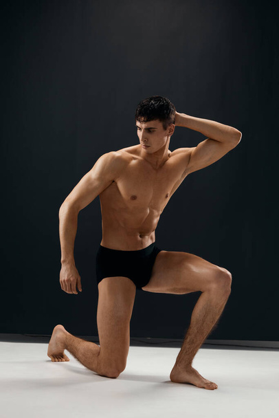 sexy man in black panties is kneeling with a pumped-up body studio - Foto, afbeelding