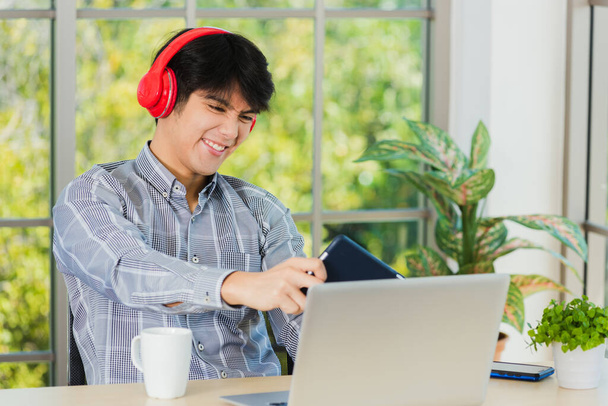 Asian young business man with red headphones he sitting on desk workplace using digital tablet play racing online video games, confident handsome man lifestyle he smiles and funny - Foto, Bild