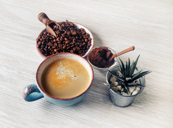 Photo of fresh tasty coffee on light wood table background. Coffee cup, roasted coffee beans, plant and ground powder. - Fotó, kép