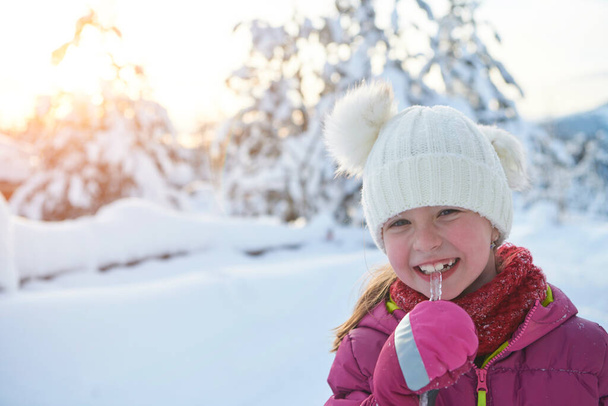 portrait of cute little girl  while eating icicle  on beautiful winter day with fresh snow - Photo, Image