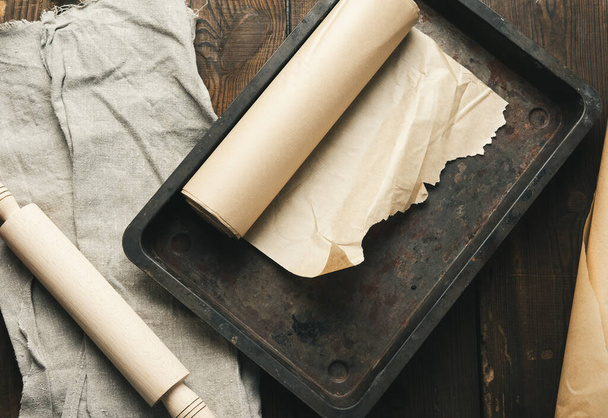 prázdná obdélníková kovová pánev potažená hnědým pergamenovým papírem a papírovými role na dřevěném stole, horní pohled - Fotografie, Obrázek