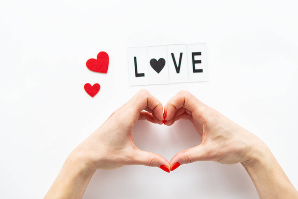 Female hands in the shape of a heart isolated on a white background, side view of small red hearts. Love lettering - Photo, Image