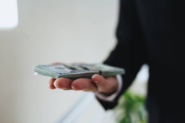One hundred dollar bills money bundle, in hand of man in suit and white shirt. Blurred background. High quality photo - Foto, Bild