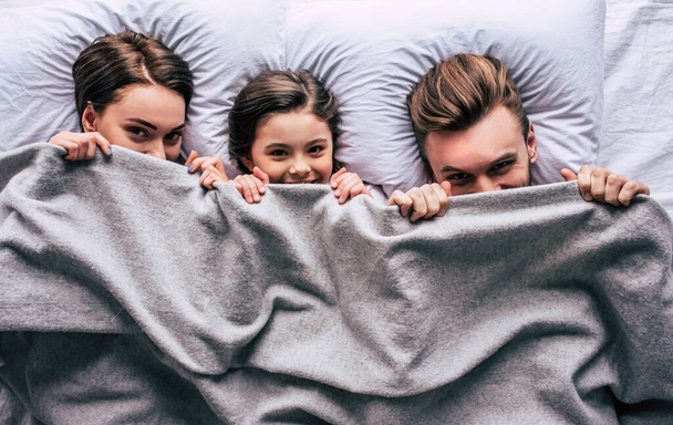 Счастливая семья лежит под одеялом - Фото, изображение