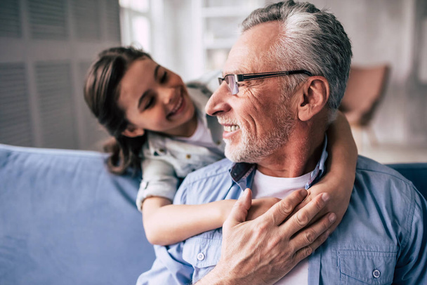Szczęśliwa dziewczyna przytula dziadka na kanapie - Zdjęcie, obraz