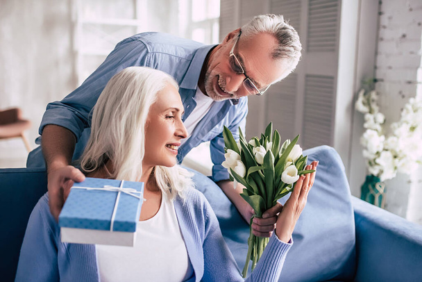 The happy elderly man giving flowers and a gift to a woman - Photo, Image