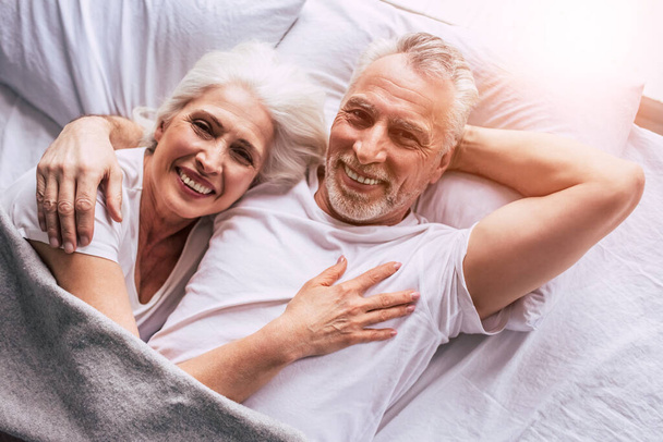 The smiling elderly couple laying on the bed - Foto, afbeelding