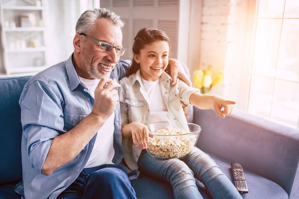 Το κοριτσάκι και ο παππούς βλέπουν τηλεόραση με ποπ κορν. - Φωτογραφία, εικόνα