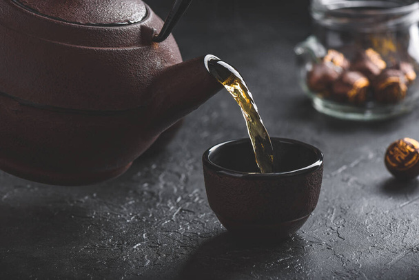 Pouring ready red tea from iron kettle into tea bowl - Foto, Imagen