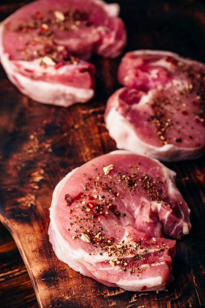 Raw pork loin steaks with different spices on rustic cutting board - Fotoğraf, Görsel