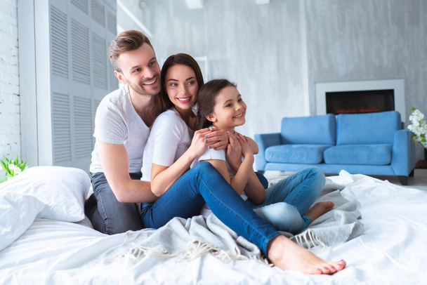 The happy parents with a girl sitting on the bed - Photo, Image