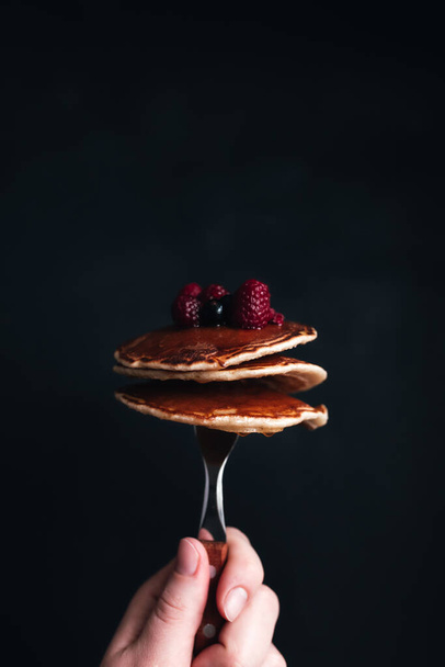 Hand holds a fork with juicy pancakes with berries and honey. High quality photo - Photo, image