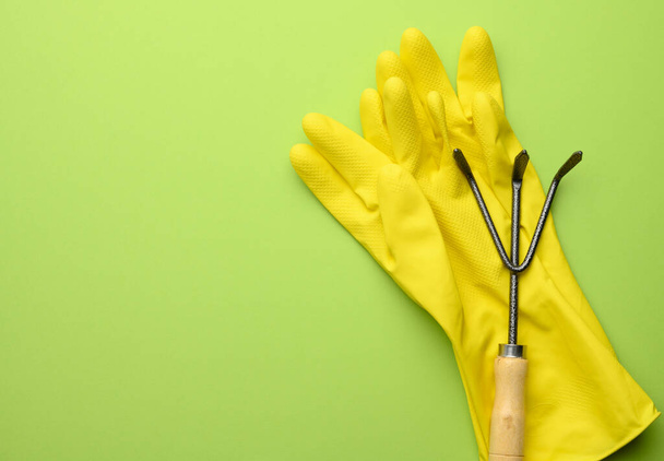 yellow rubber gloves and metal garden small rake on green background, copy space - Φωτογραφία, εικόνα