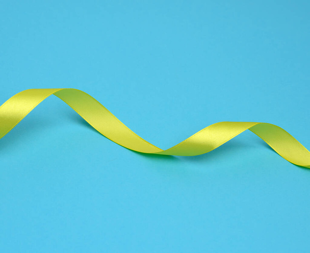 curled yellow silk ribbon on a blue background, copy space - Фото, изображение