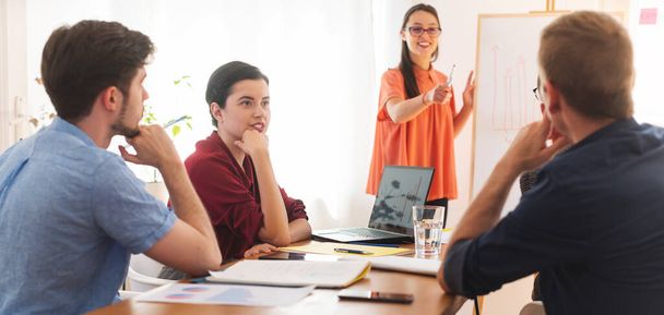 Sonriendo colega mujer informar estrategia de negocio a sus otros colegas de oficina en pizarra blanca - Foto, imagen