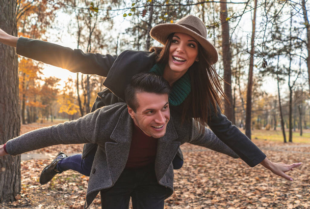 El hombre que lleva a la mujer en la espalda en el parque de otoño - Foto, imagen