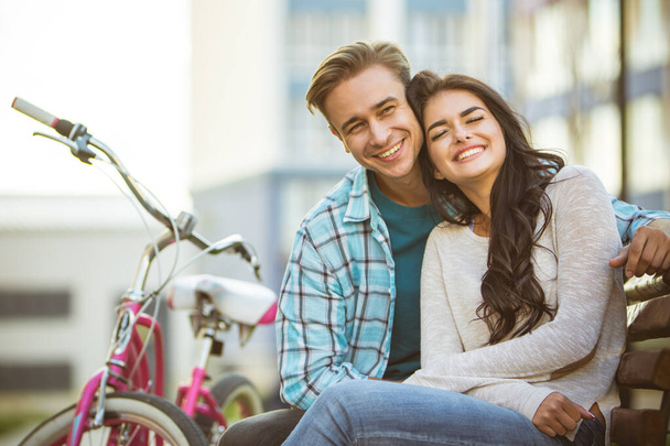 La coppia sorridente siede sulla panchina vicino alle biciclette - Foto, immagini