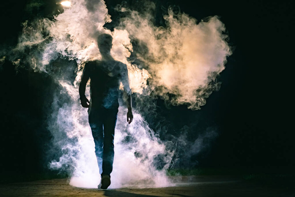 Чоловік ходить у диму на чорному тлі
 - Фото, зображення