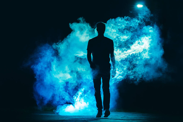 Samiec chodzący w niebieskim dymie na ciemnym tle. wieczorna noc - Zdjęcie, obraz