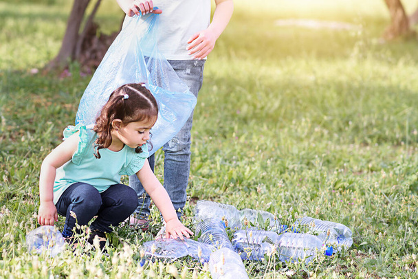 Τα παιδιά καθαρίζουν στο πάρκο. Εθελοντικά παιδιά με σακούλα σκουπιδιών να καθαρίζει σκουπίδια, να βάζει πλαστικό μπουκάλι σε σακούλα ανακύκλωσης. - Φωτογραφία, εικόνα