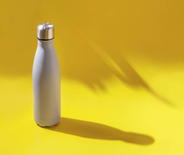 Close-up of grey reusable steel bottle on yellow background with hard light - Фото, изображение