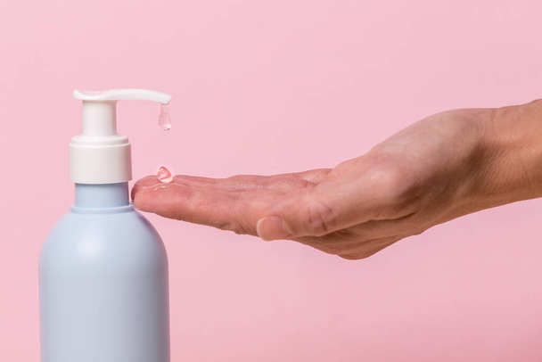 Female hand using alcohol gel sanitizer bottle dispenser, against coronavirus disease (Covid-19) . Antiseptic, Hygiene and Health concept. Minimalist style on pink background - Foto, Imagem
