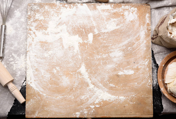 белая пшеничная мука, деревянная скалка и старая разделочная доска на столе, вид сверху - Фото, изображение