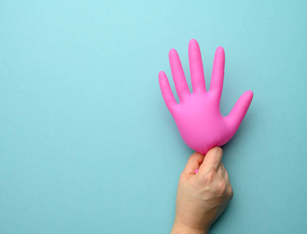 female hand holding rubber pink inflated glove on blue background, copy space - Foto, afbeelding