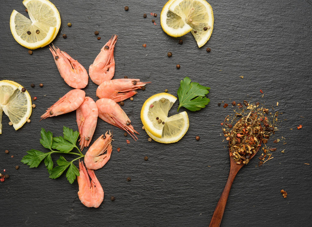 fresh shrimp and lemon slices on black board, top view - Фото, изображение