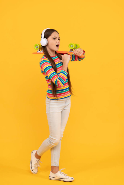 серйозна дитина в навушниках з дошкою для пенні. Дівчина-підліток слухає музику. дитяча діяльність
. - Фото, зображення