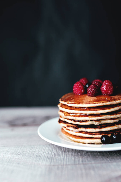 Juicy pancakes with berries and honey on a white plate, spoon, wooden table. High quality photo - Foto, Imagem