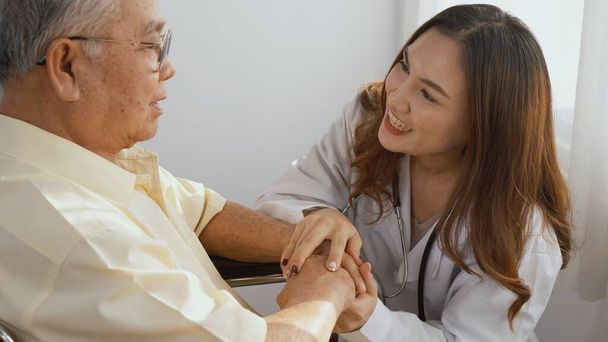 Female nurse doctor wear white uniform holding hand of patient senior or elderly old man during sit on wheelchair encourage and empathy at nursing hospital, older people healthcare support concept - Photo, image