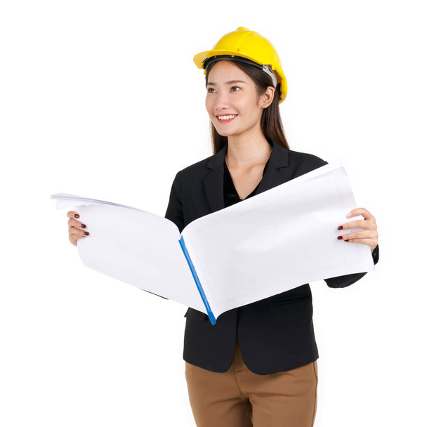 Young businesswoman in black suit, wearing a yellow construction helmet, unfolds the construction plan, looking out in the distance. - Foto, Imagen