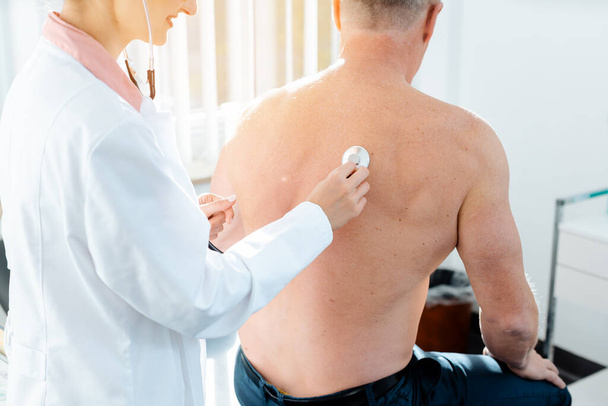 Doctor using stethoscope to check lung function on back of man - Photo, Image
