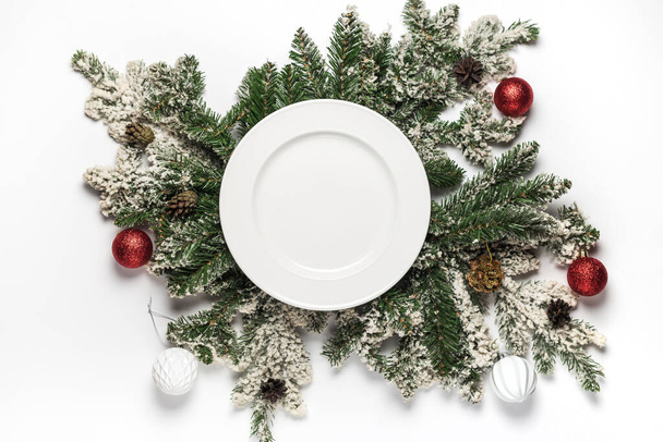 Κενό λευκό κεραμικό πιάτο με κλαδιά ελάτης και διακόσμηση. Επίπεδη θέσει Χριστούγεννα και το νέο έτος έννοια. Άνω όψη. - Φωτογραφία, εικόνα