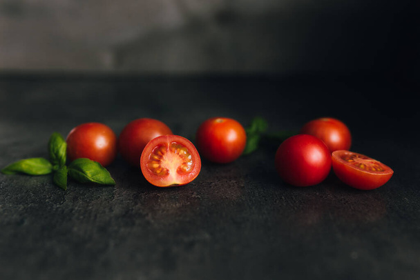 Tomates de cereja vermelhos com manjericão verde em um fundo cinza. Foto de alta qualidade - Foto, Imagem