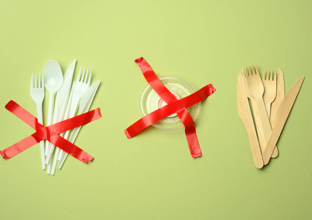 plastic forks and spoons glued with red tape on a green background, avoiding plastic, preserving the environment - Foto, imagen