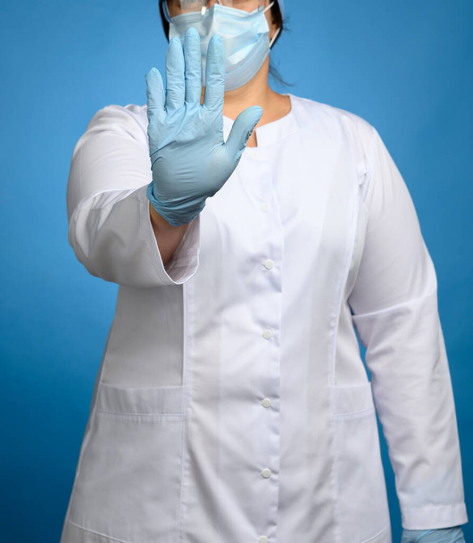 doctor in white medical coat and blue latex gloves shows stop gesture, concept of keeping a safe distance, do not panic - Фото, изображение