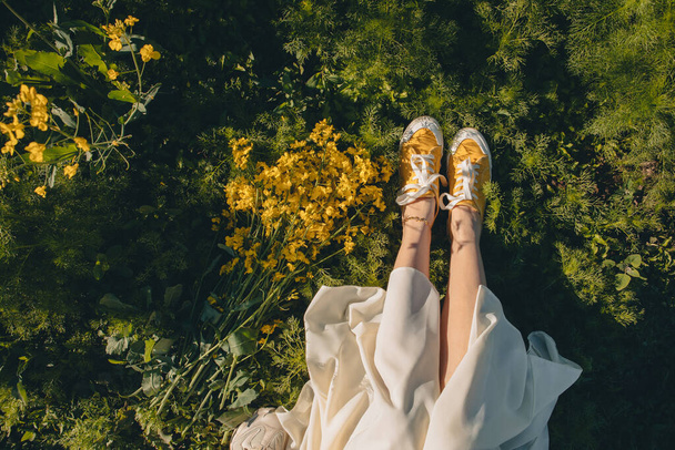 donna in scarpe gialle seduto in erba vicino colza parte del corpo bouquet - Foto, immagini