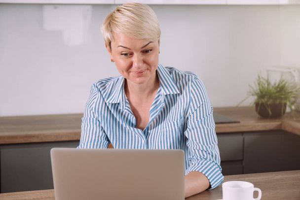 Zakelijke vrouw werkt via laptop zitten in de keuken thuis, freelancer werkproces concept met behulp van draagbare computer - Foto, afbeelding