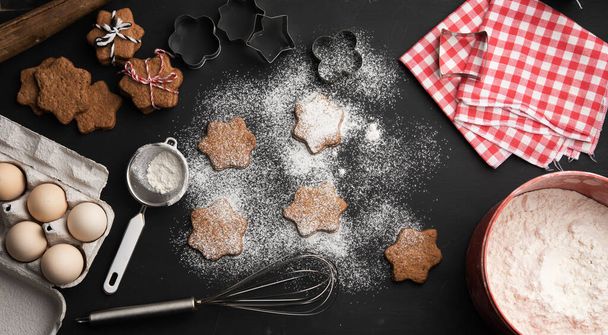 baked star-shaped gingerbread cookie sprinkled with powdered sugar on a black table and ingredients, top view - Foto, Imagen