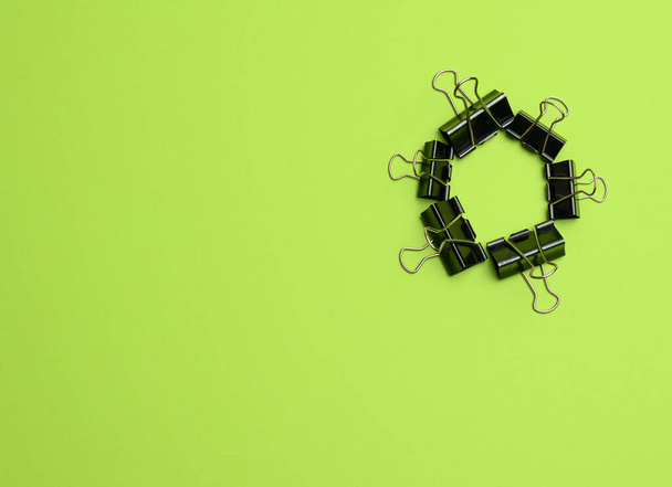 stack of black metal stationery clips on a green background, top view - Фото, зображення