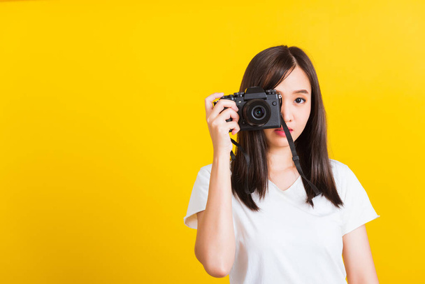 Portrait of happy Asian beautiful young woman photographer taking a picture and looking viewfinder on retro digital mirrorless photo camera ready to shoot, studio shot isolated on yellow background - Photo, Image
