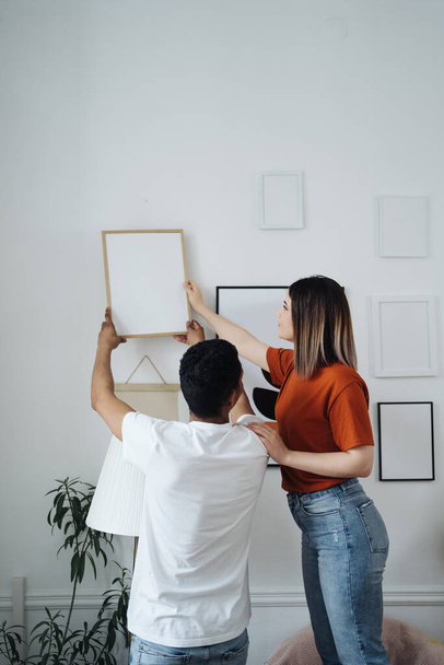 Mixed race ethnicity millennial couple holding frame admires painting or photo - Photo, Image