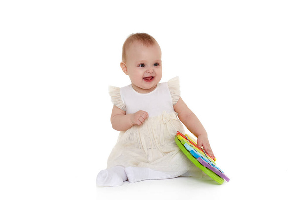 Sweet baby in dress  plays with colourful  xylophone (musical instrument  toy for children) on a white background. Early development and learning toys. Eight months - Photo, Image